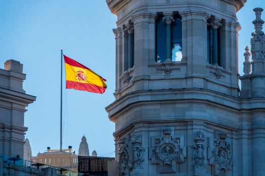 Flag of Spain waving next to historic architecture in Madrid.